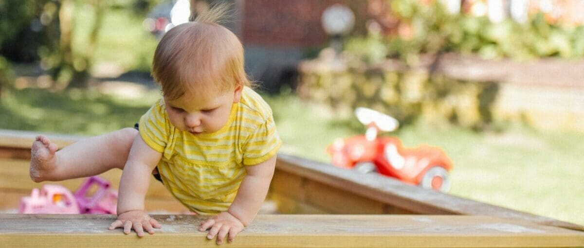 Toddler Playing in a Sandbox Outside - Climbing Out